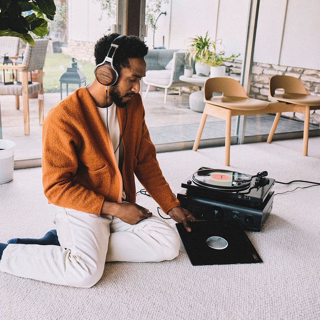 man listening to Denon record player sitting on floor