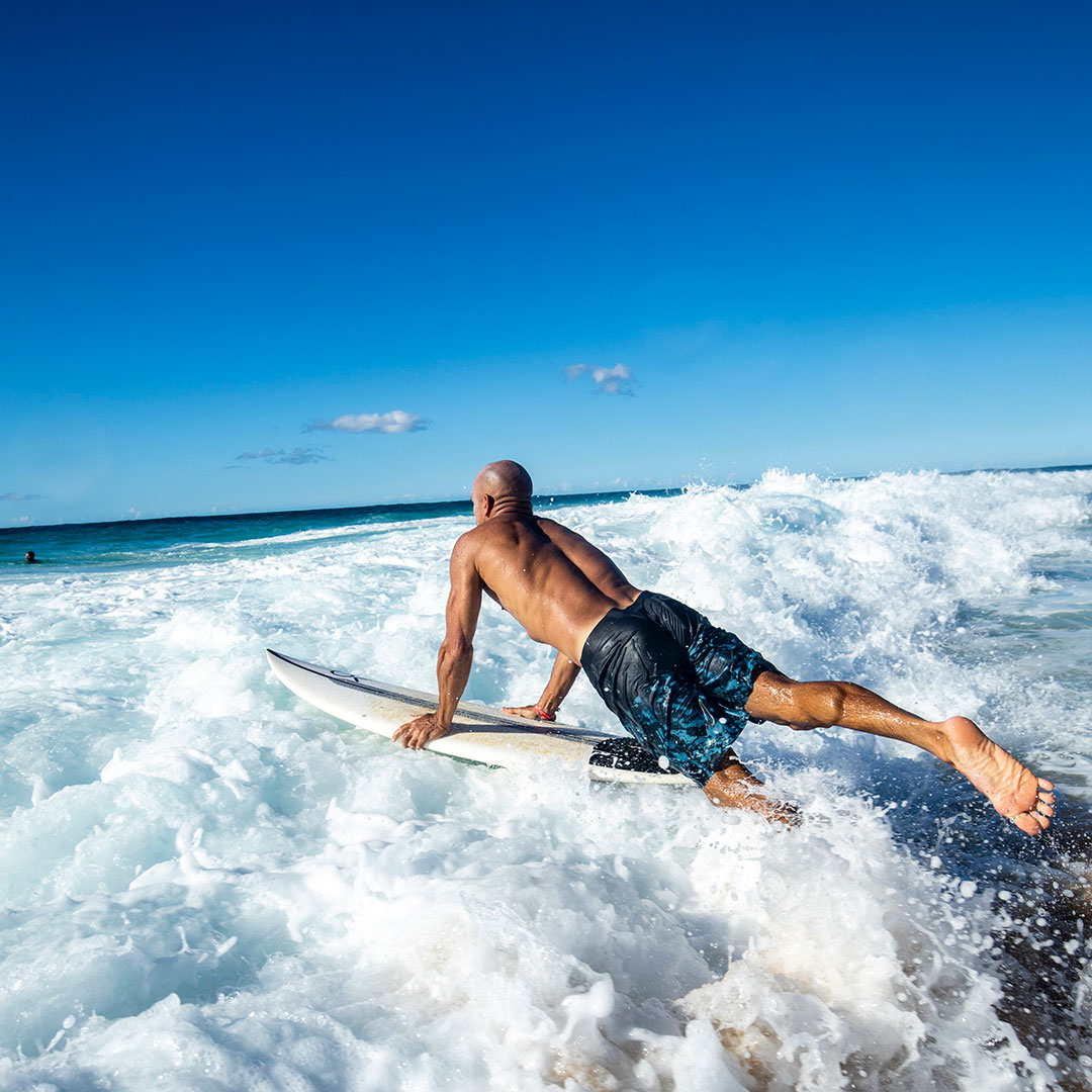 Outerknown brand shot - Professional Surfer Kelly Slater jumping into ocean with surfboard