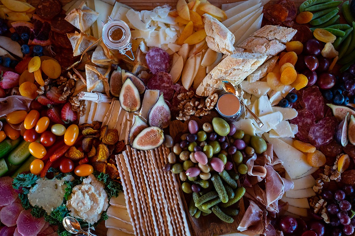 A charcuterie board by Land Charc Provisions with cheeses, bread, figs, dates, nuts, olives, tomatoes, and more. 