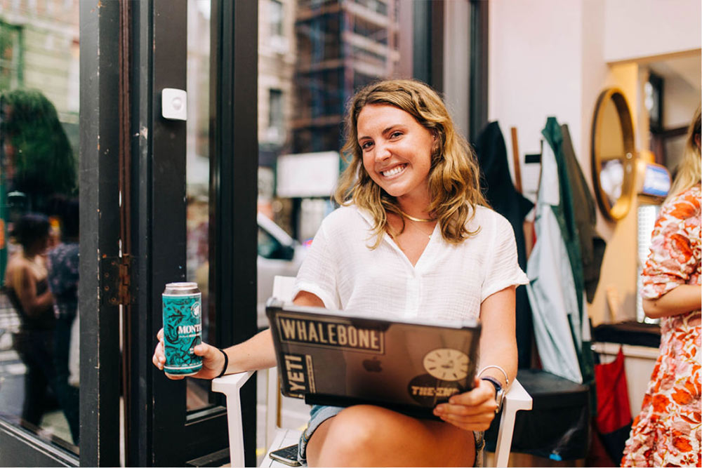 women sitting with a laptop in her lap and holding a montauk brew co beer can
