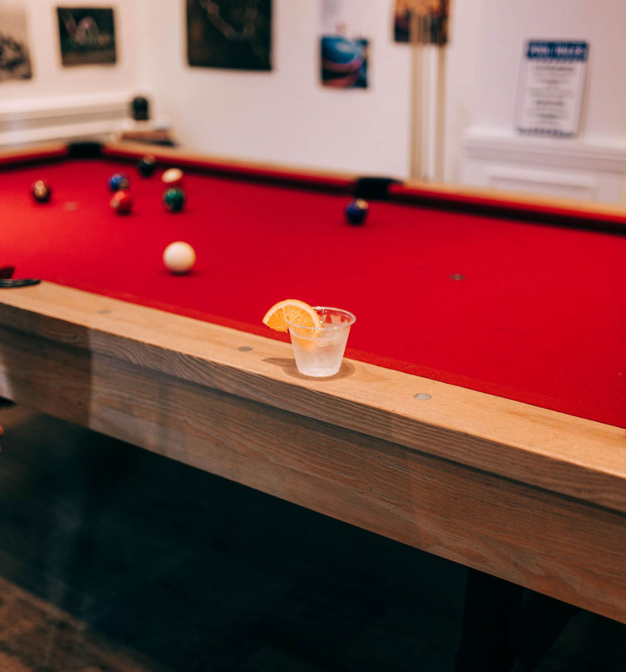A drink sitting on the edge of a pool table