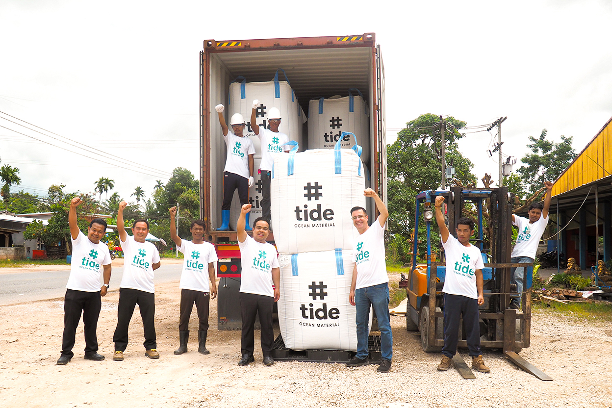 Tide team smiling with fists raised with big bags of recycled plastics