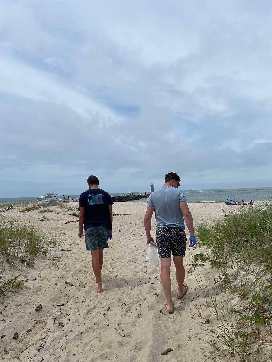 Two men walk onto the beach looking for trash during the Fair Harbor Gin Beach Cleanup and Happy Hour in Montauk