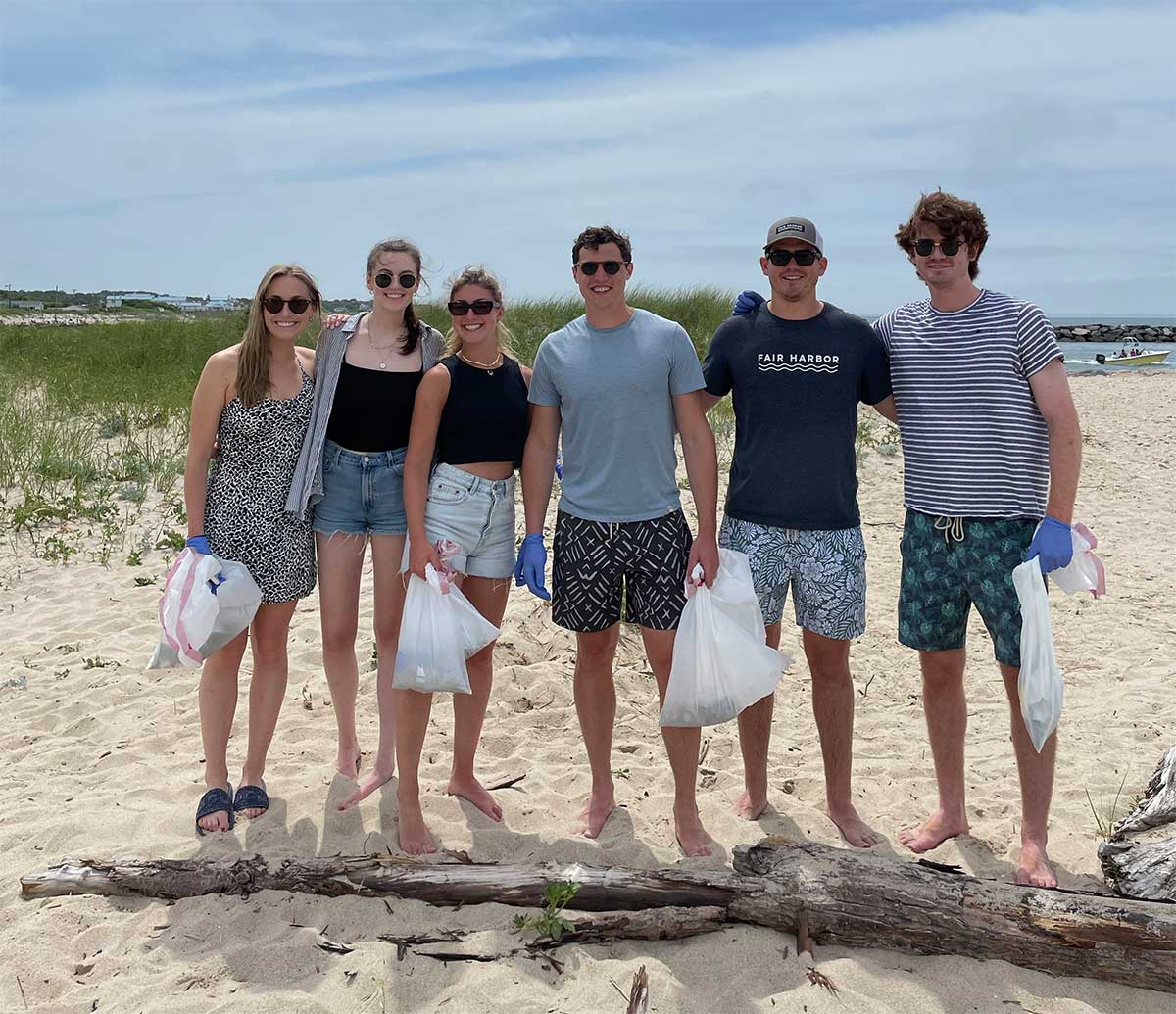A group on of people stand together and smile for a photo during the Fair Harbor Gin Beach Cleanup and Happy Hour in Montauk