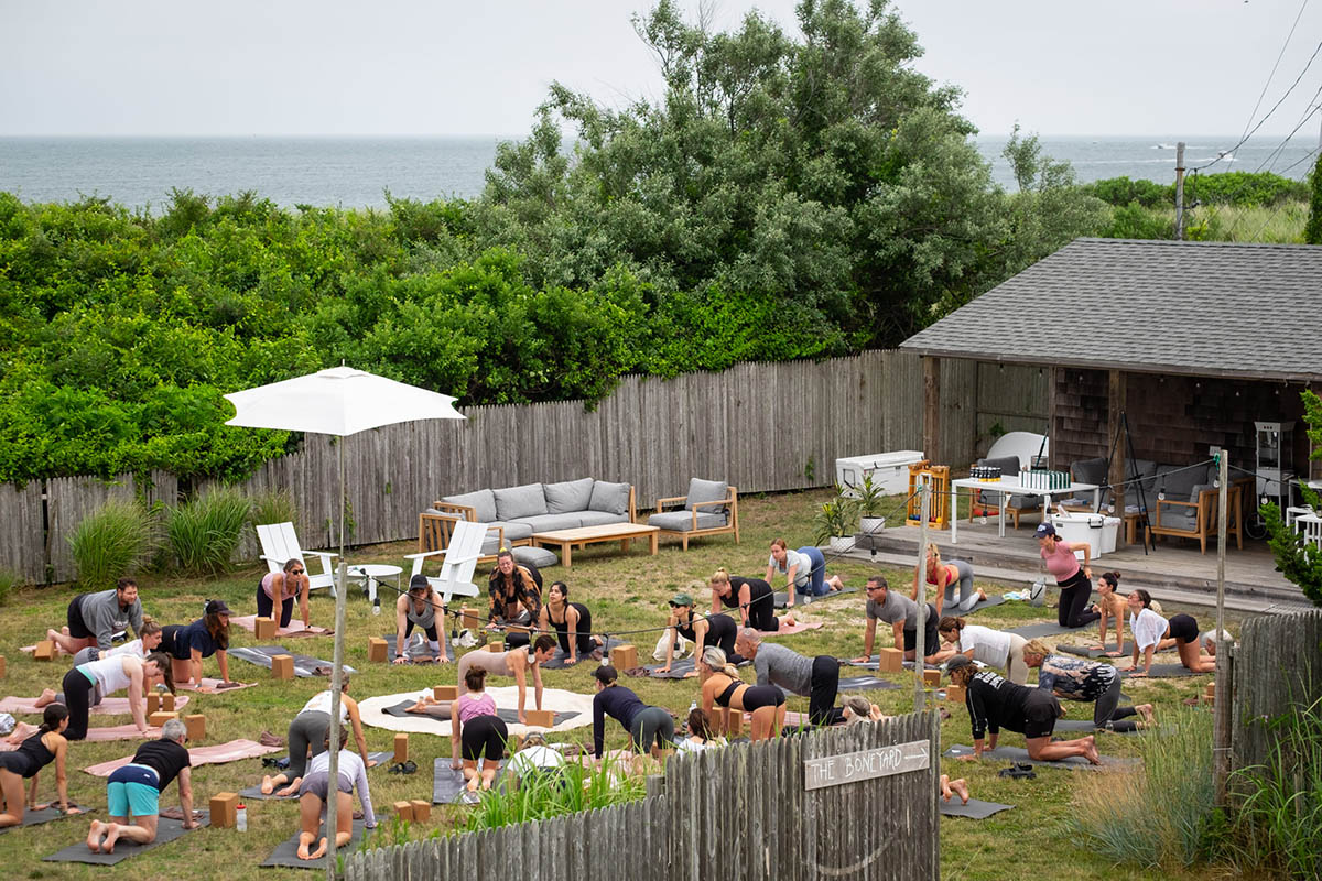 A large group of people participate in a yoga class during the Fair Harbor Gin Beach Cleanup and Happy Hour in Montauk