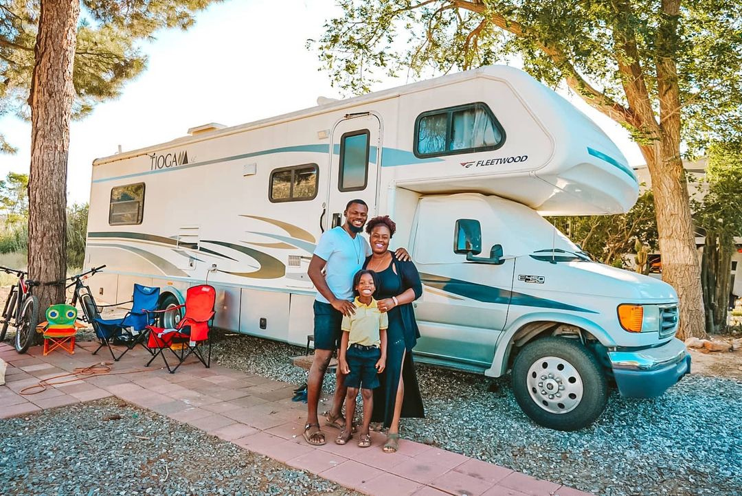 Two adults and a child, all smiling, stand in front of Fleetwood Tioga RV.