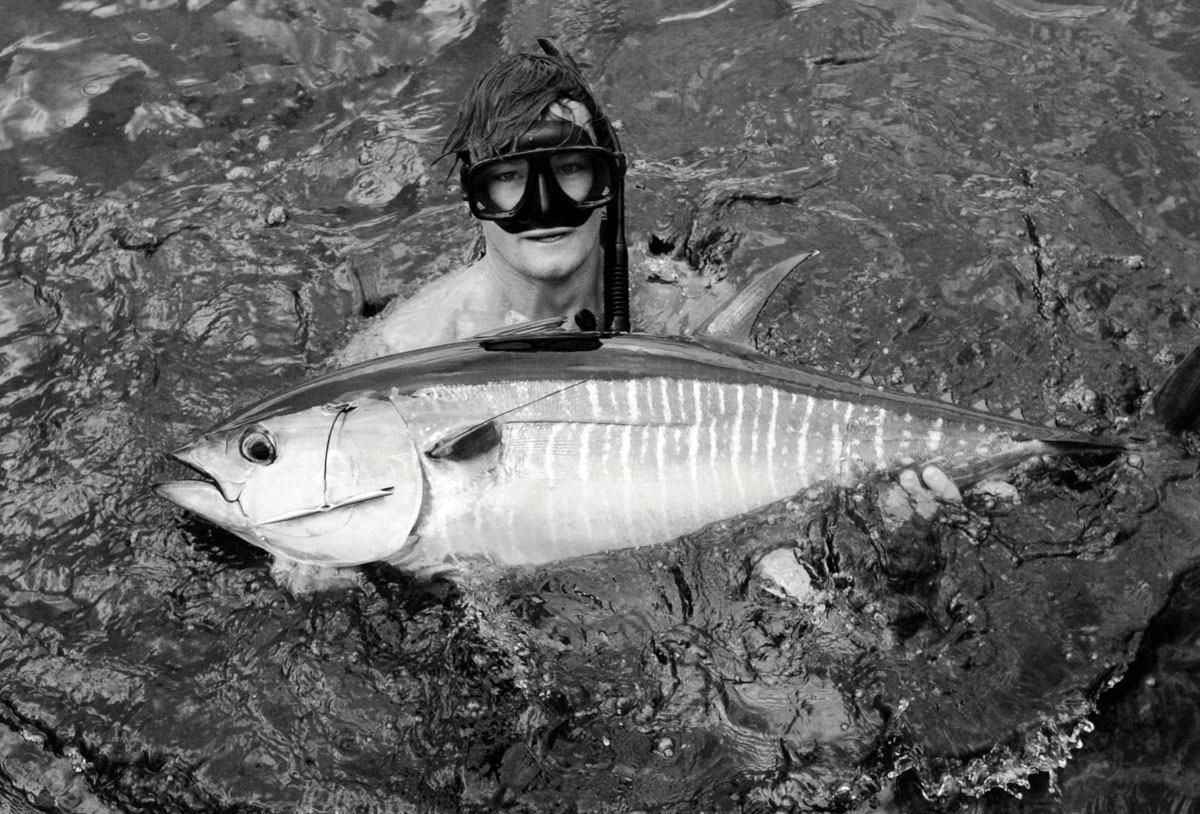 Black and white photograph of Justin Burkle wearing a snorkeling mask, in water, holding a large fish.