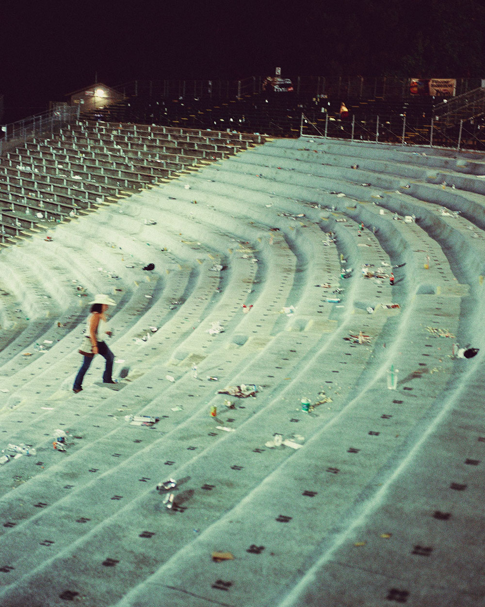 An empty stadium with trash and liter. A woman wearing a cowboy hat walks up the steps In photograph of Folsom Rodeo 60th Anniversary by Cameron Munn