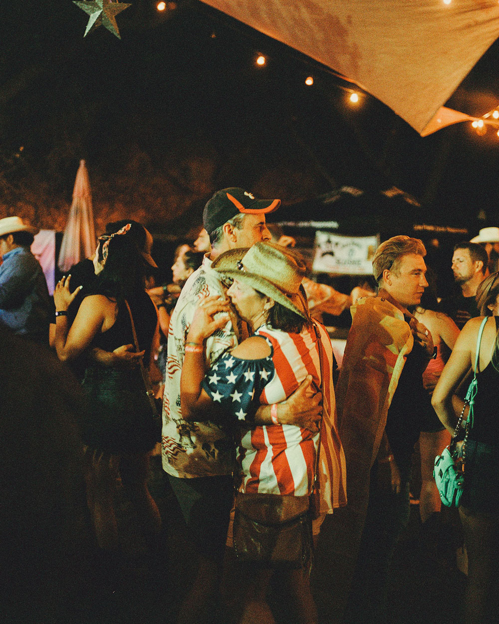An older couple dance at night. The woman is wearing an American flag shirt In photograph of Folsom Rodeo 60th Anniversary by Cameron Munn