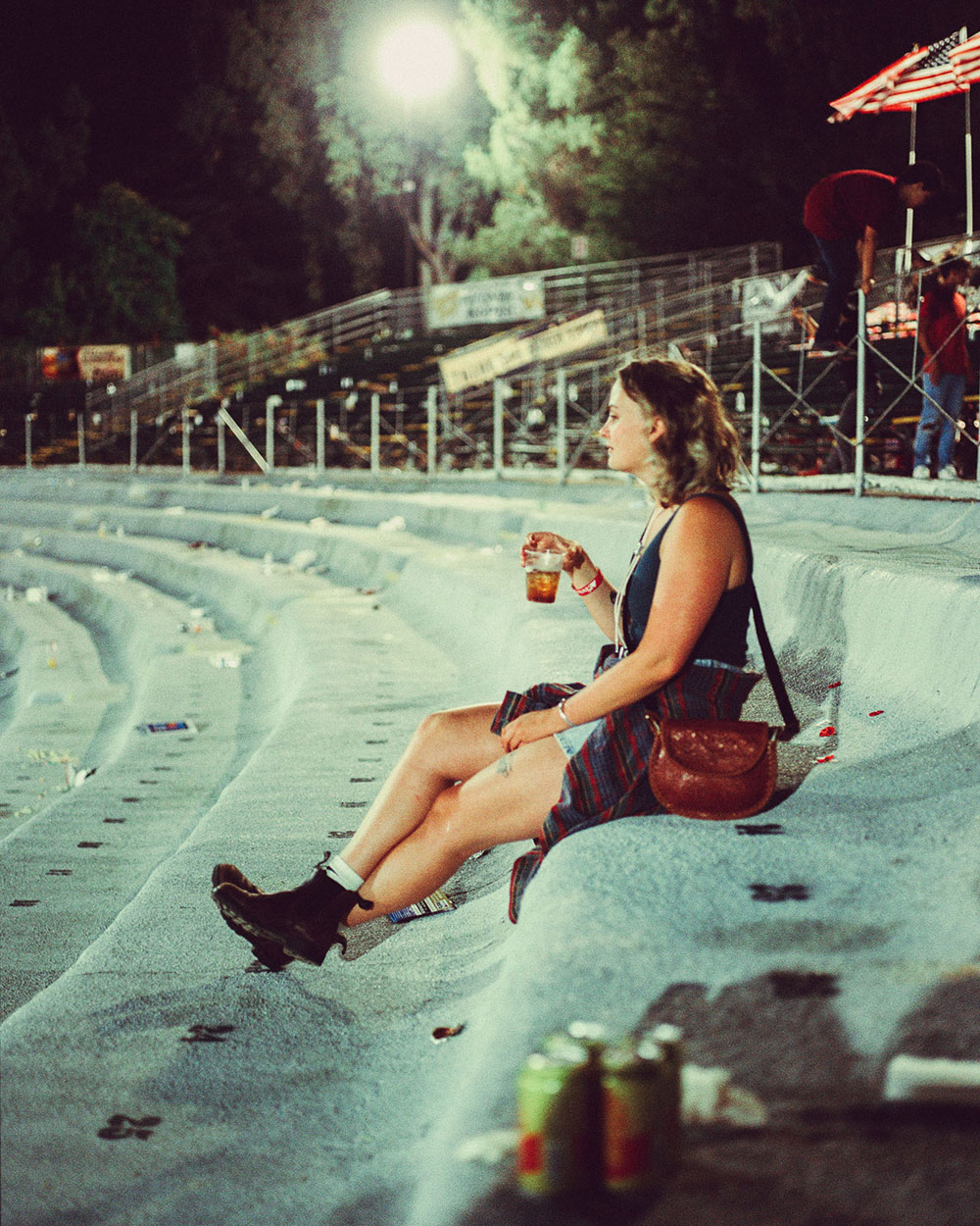 A woman site alone in an empty stadium, holding a cup of beer In photograph of Folsom Rodeo 60th Anniversary by Cameron Munn