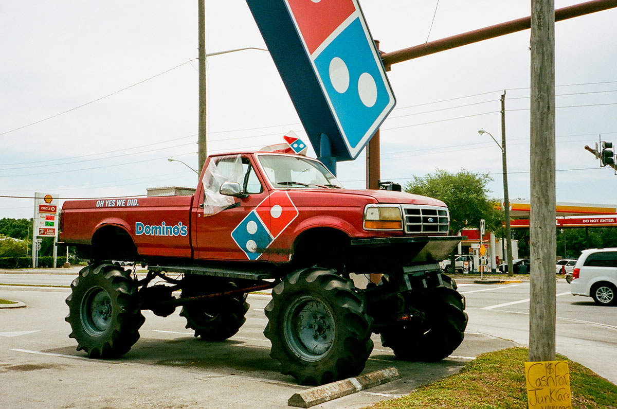 Photograph by Gunner Hughes of a lifted red Domino's Pizza Truck and parked underneath a domino's sign