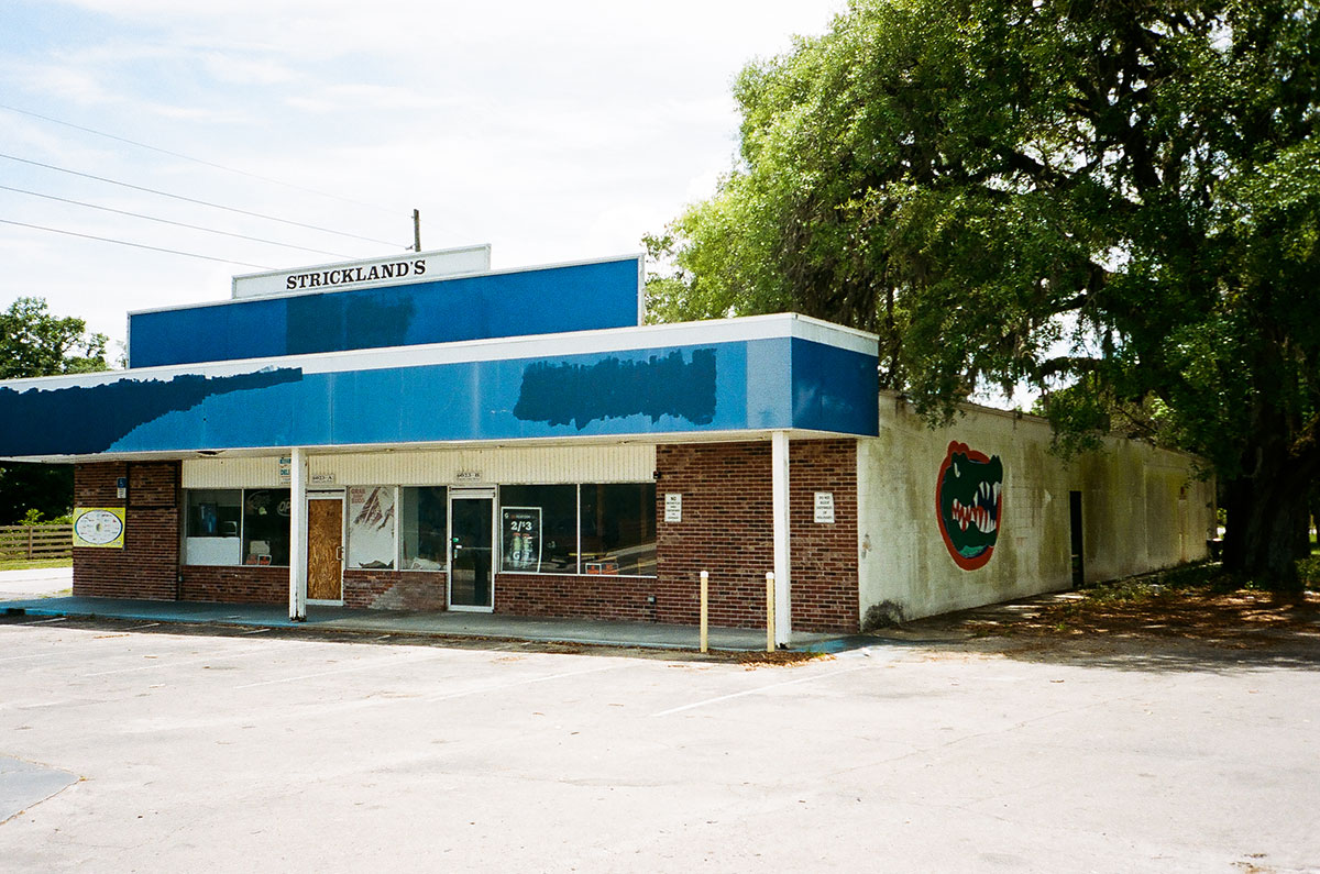 Photograph by Gunner Hughes of an abandoned storefront. The UF gator logo is painted on the side white wall.