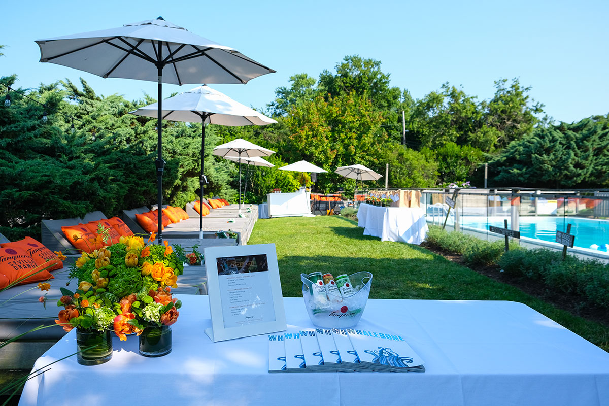 Tanqueray event at Sole East in Montauk. Table with drinks and magazine sits in the foreground. In the background is a lawn, pool, and lounge chairs and umbrellas.
