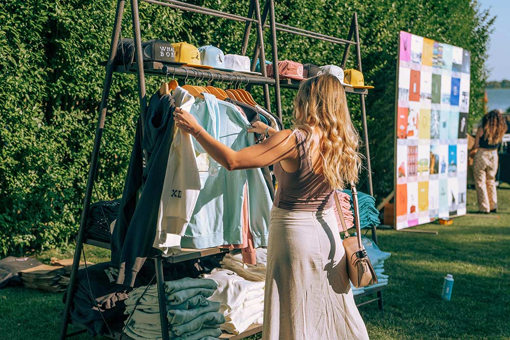 A woman with long blonde hair looking over clothing hanging on a rack at the Whalebone Magazine Sixth Anniversary party at the Montauk Lake House