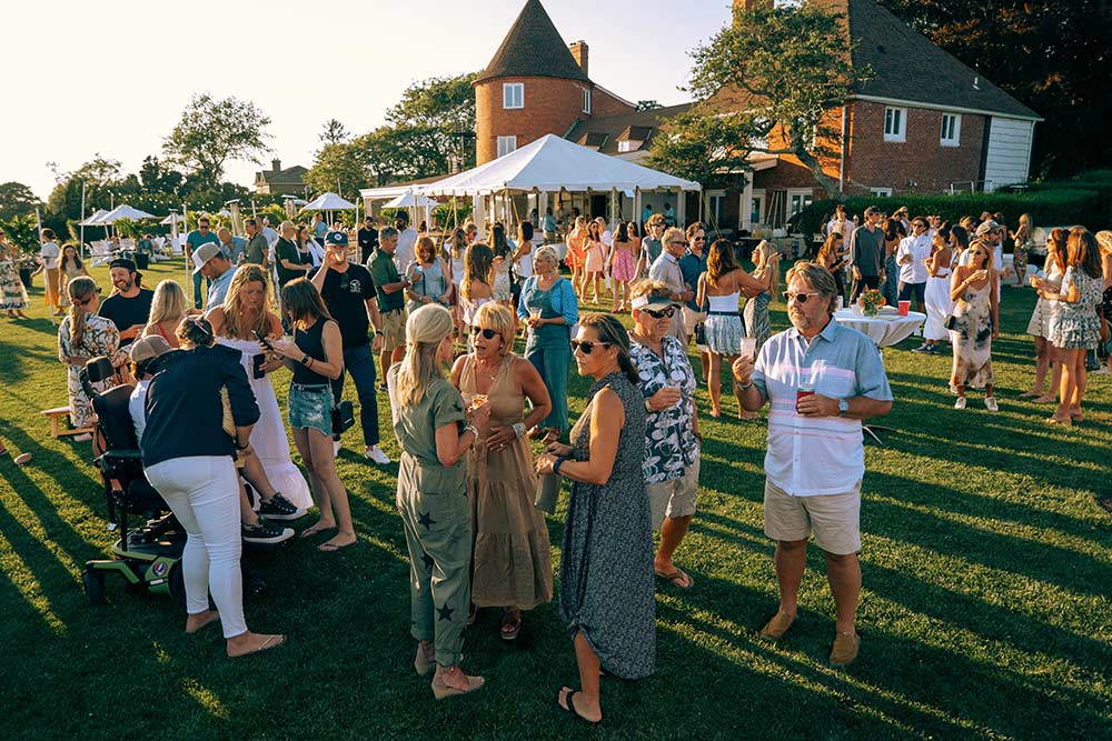 A large group of people standing on a lawn in the setting sun at the Whalebone Magazine Sixth Anniversary party at the Montauk Lake House