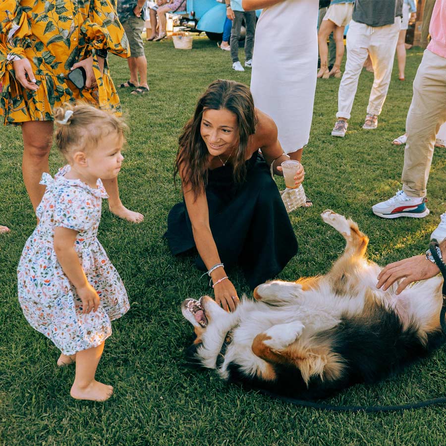 A woman and a little girl reach down to pet a dog laying on his back at the Whalebone Magazine Sixth Anniversary party at the Montauk Lake House