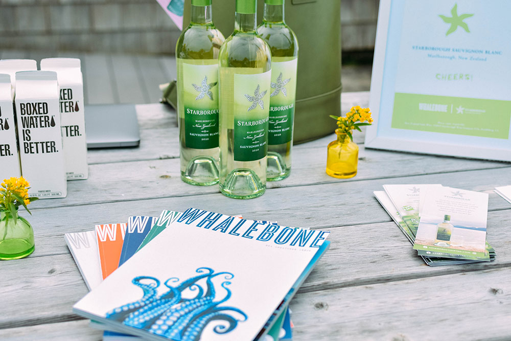 Bottles of Starborough wine, boxed water and whalebone magazines sit on a wood table outside.