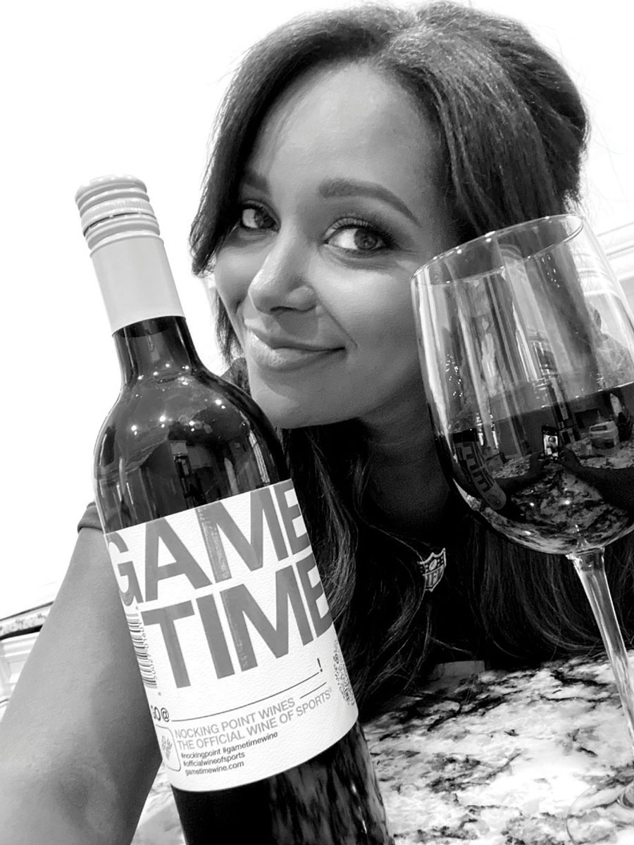 Brandi Rhodes smiling with a bottle and a poured glass of red Nocking Point wine.