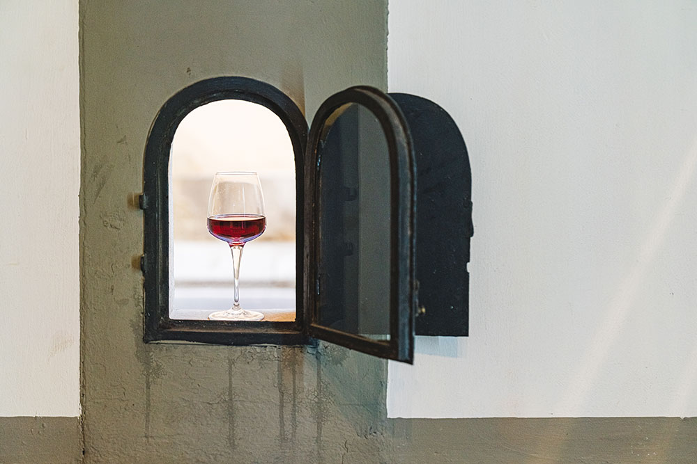 A clear glass of red wine sits in an open wine window in Florence, Italy