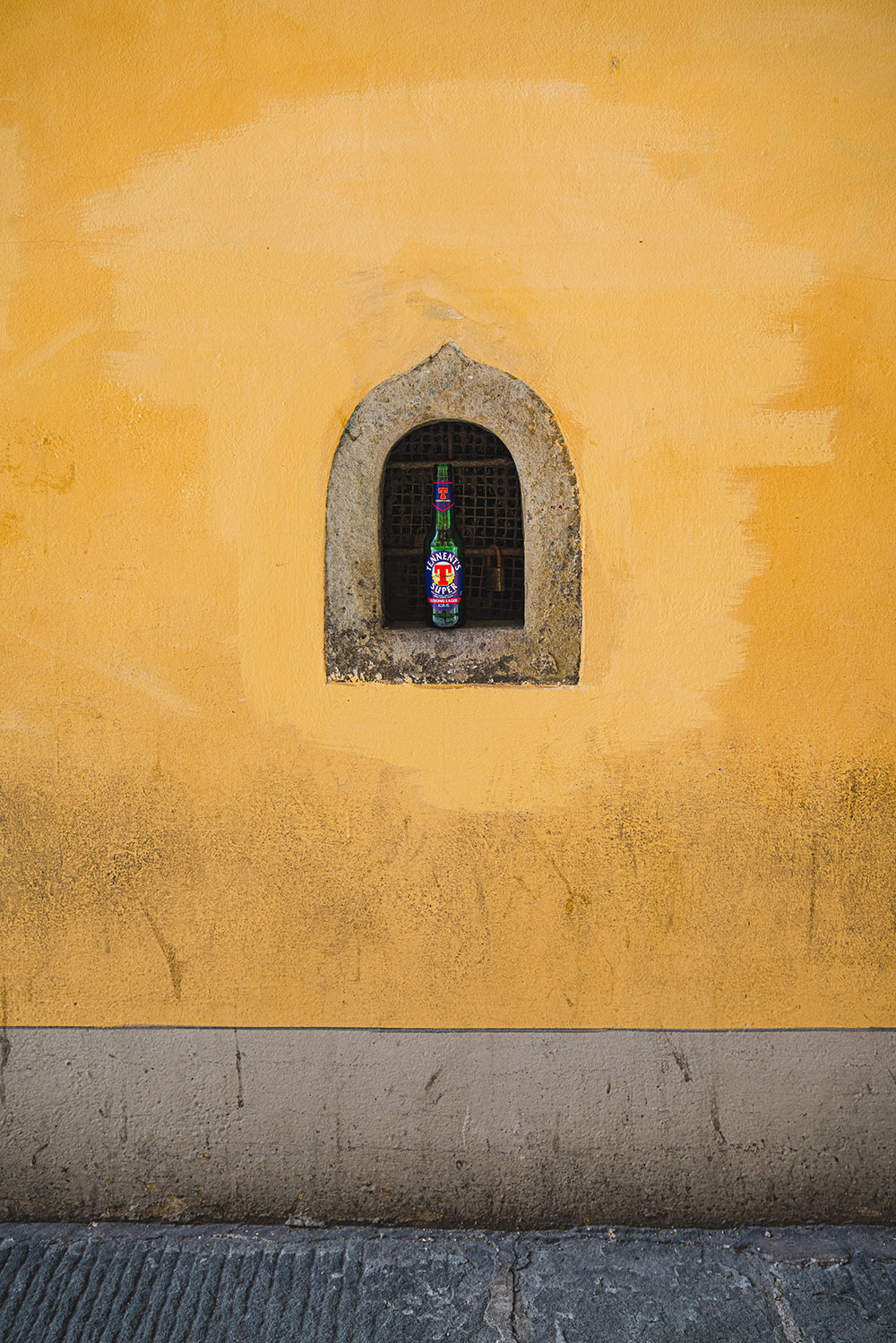 A bottle sits in a a wine window in Florence, Italy in a yellow wall