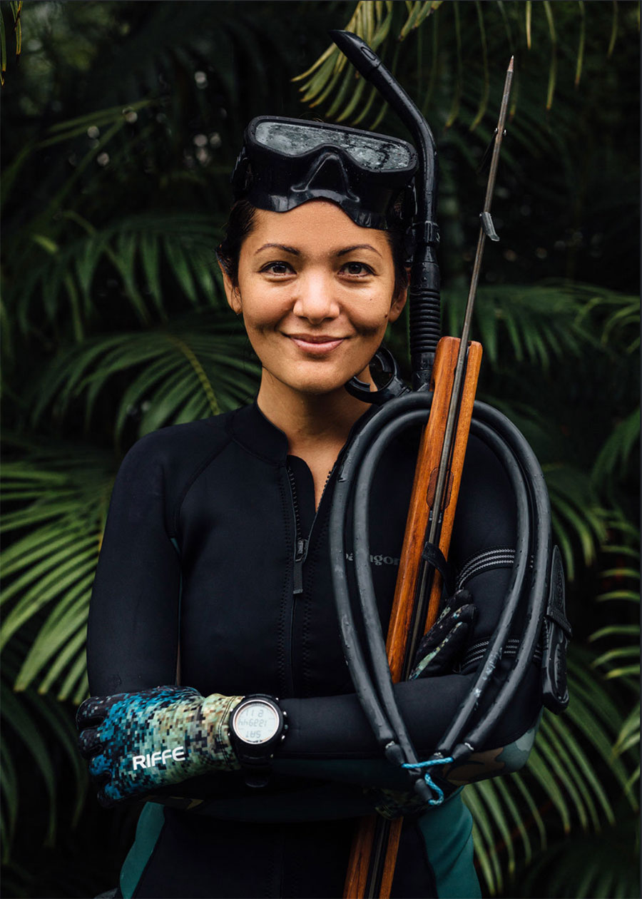 Photograph of Kimi Werner for Gear Patrol, taken by Chase Pellerin. Kimi wears a wet suit, goggles, and holds a spear gun against a backdrop of palms.
