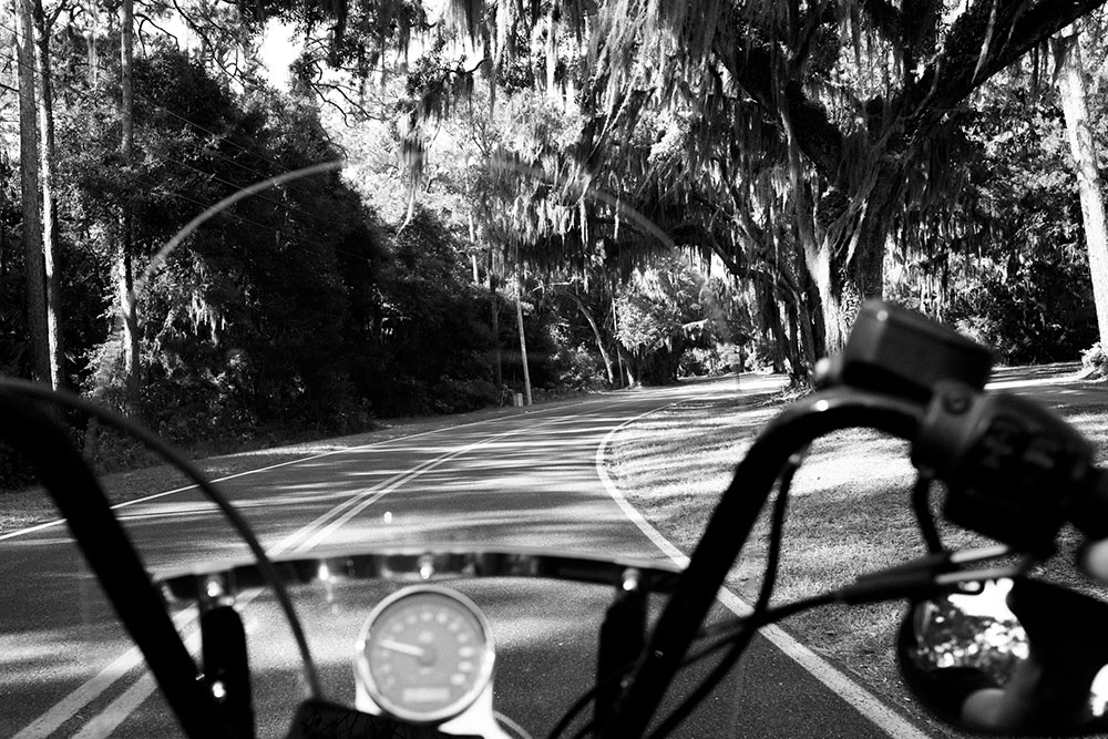 Black and White photo of handle bars of motorcycle on open road taken by Gunner Hughes