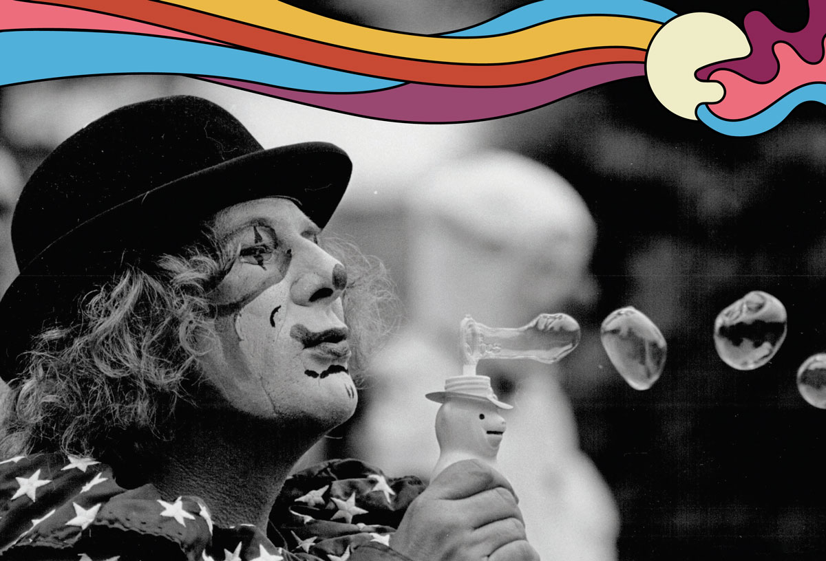 Black and white photo of Wavy Gravy as a clown, blowing bubbles