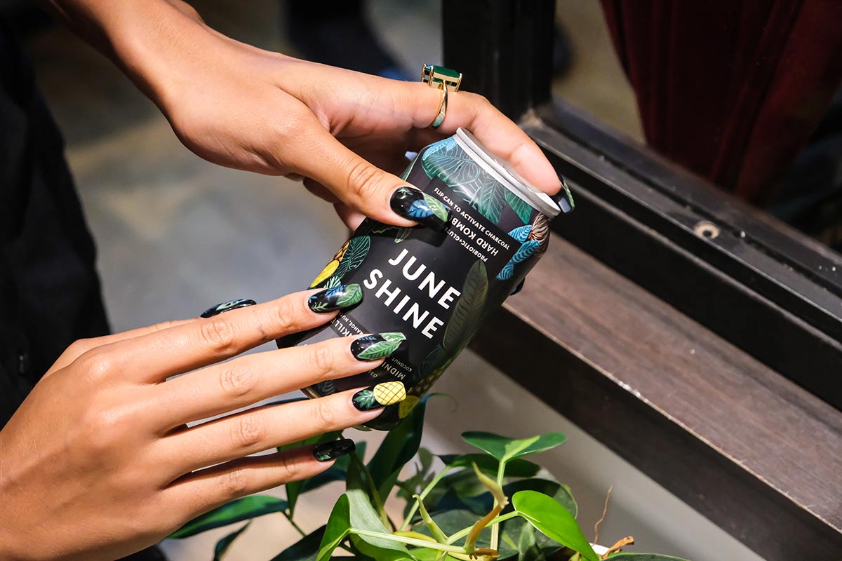 A woman holds a can of JuneShine and compares her nail art to the can design at the Governors Ball pre-game bash with JuneShine and Whalebone Magazine on Bleecker Street.