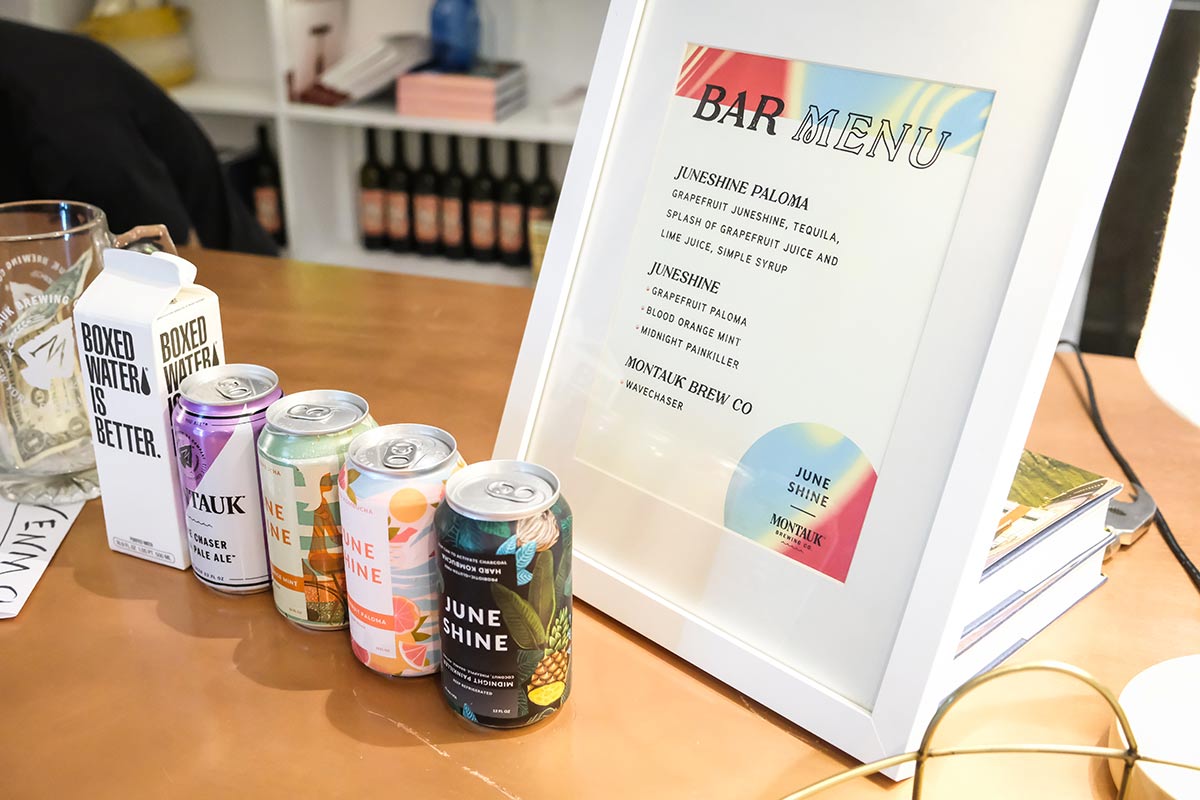 Boxed water and cans of drinks sit next to a printed and framed bar menu at the Governors Ball pre-game bash with JuneShine and Whalebone Magazine on Bleecker Street.