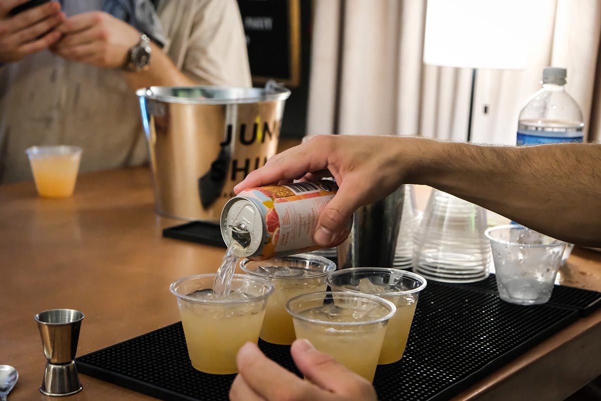 A man's hand is pouring JuneShine from a can into four small plastic cups at the Governors Ball pre-game bash with JuneShine and Whalebone Magazine on Bleecker Street.