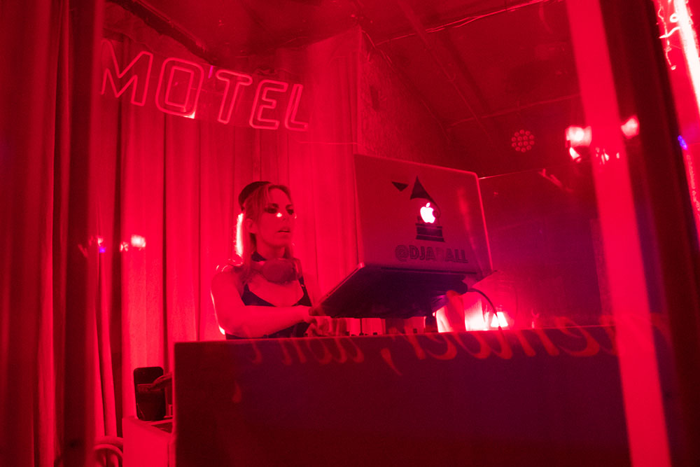 McKittrick Hotel Halloween Party 2021, DJ plays in red light in front of a neon sign