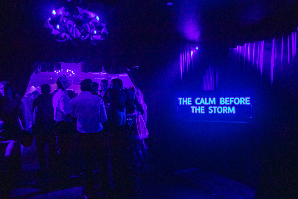 McKittrick Hotel Halloween Party 2021, guests at party and neon sign that reads the calm before the storm