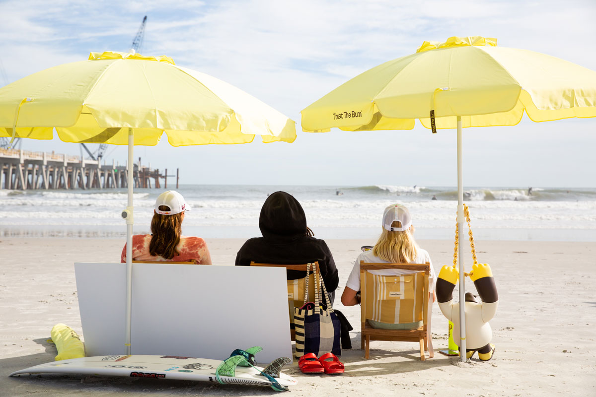 Kylie Pulcini, Gigi Lucas, Carissa Moore sitting on the beach under Sun Bum umbrellas
