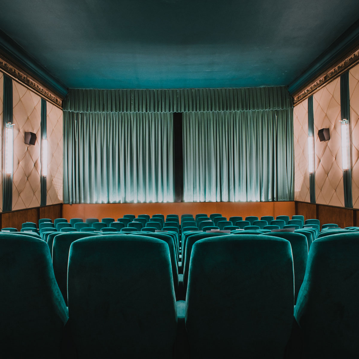 NEUES OFF KINO interior photo facing the theatre screen covered with teal velvet curtains.