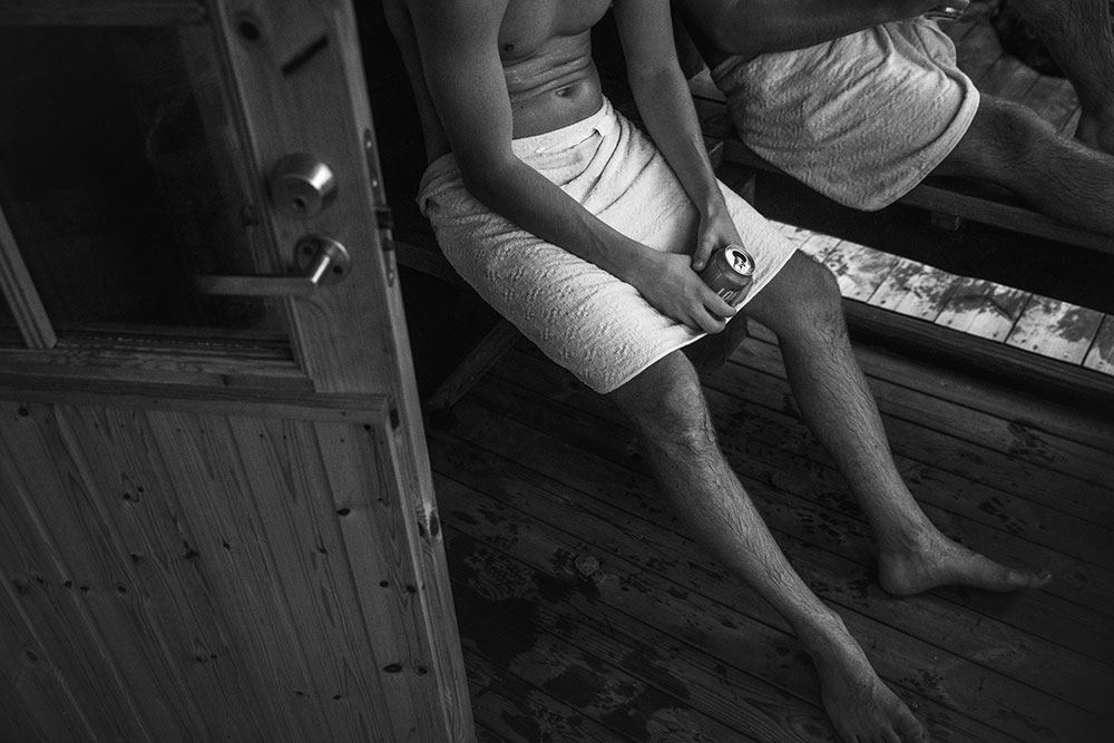Black and white image of a man holding The Long Drink in a towel by sauna door