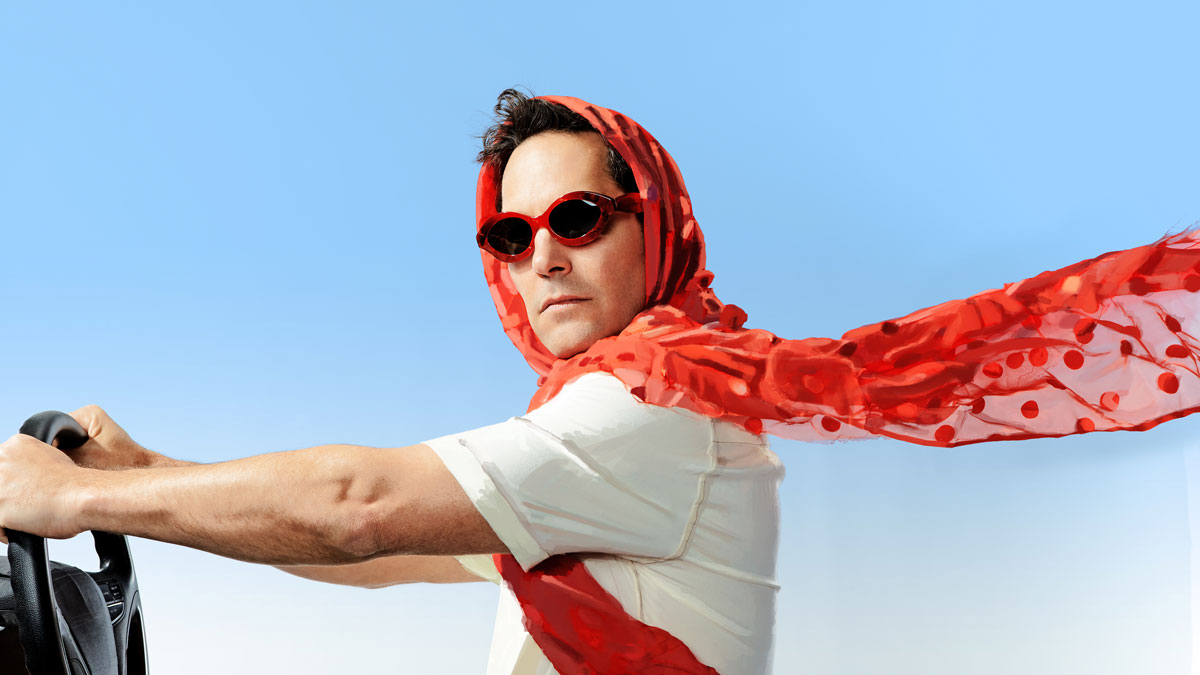 Paul Rudd with sunglasses and scarf blowing in the wind as his hands are on a steering wheel...driving?