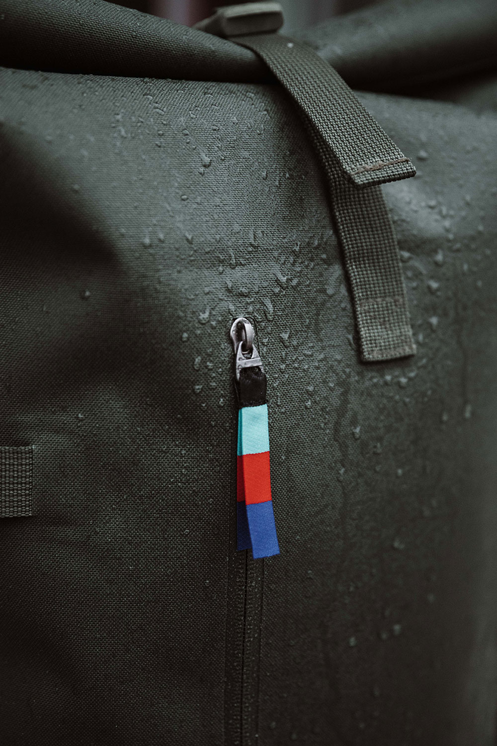 Closeup view of a GOT BAG Rolltop bag . The zipper features a tri color tag. Water beads off the sides of the water proof fabric.