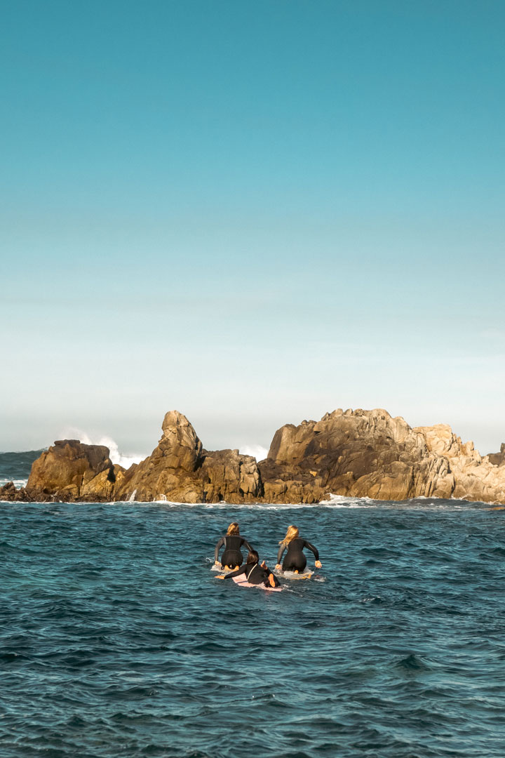 3 women paddle out towards rocks to catch a wave  by rob schanz