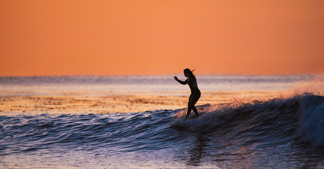 Female surfer catching a wave at sunrise  by rob schanz