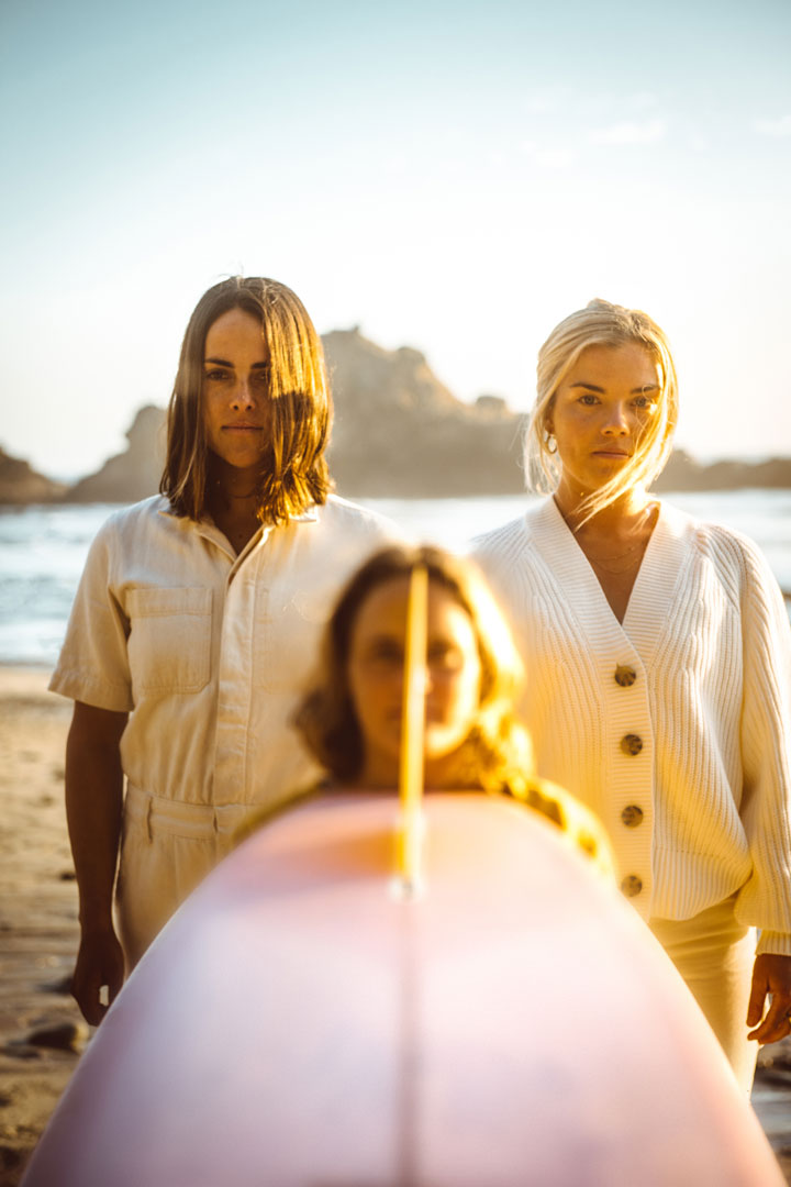 Photograph of 3 women on a beach with a surfboard  by rob schanz