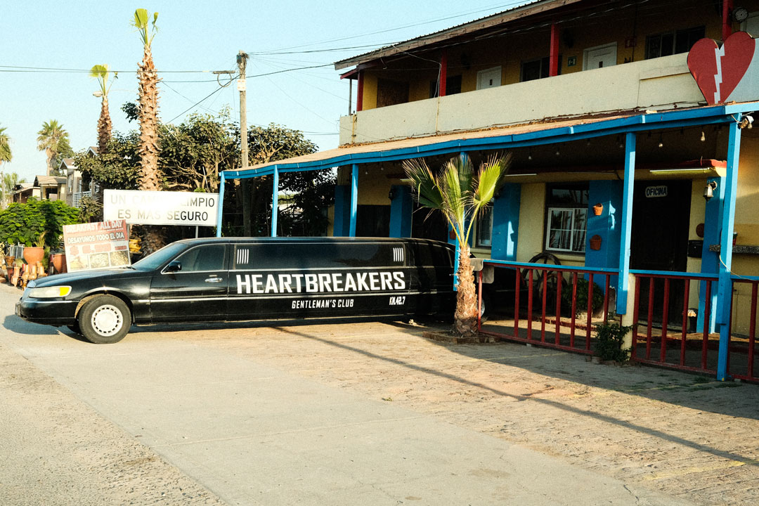 A limosuine is parked, back in, to an older blue and yellow house. The word "heartbreakers" is written across the limo.