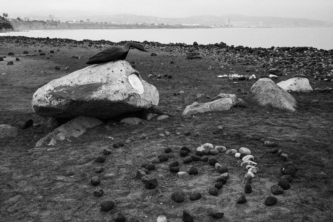 black and white photograph of beach with lots of rocks. In the foreground small rocks are arranged in a spiral