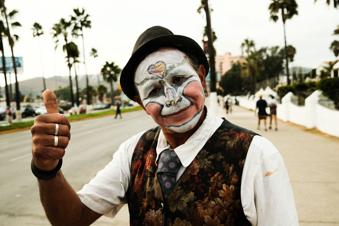 A man with a painted face and boler hat gives a thumbs up toward the camera