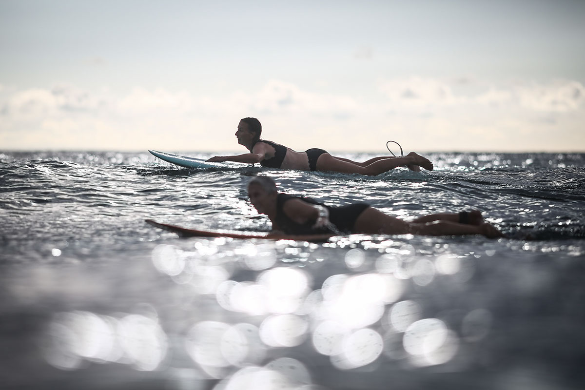 Nature of Surf Women, two women paddling on surfboards next to one another