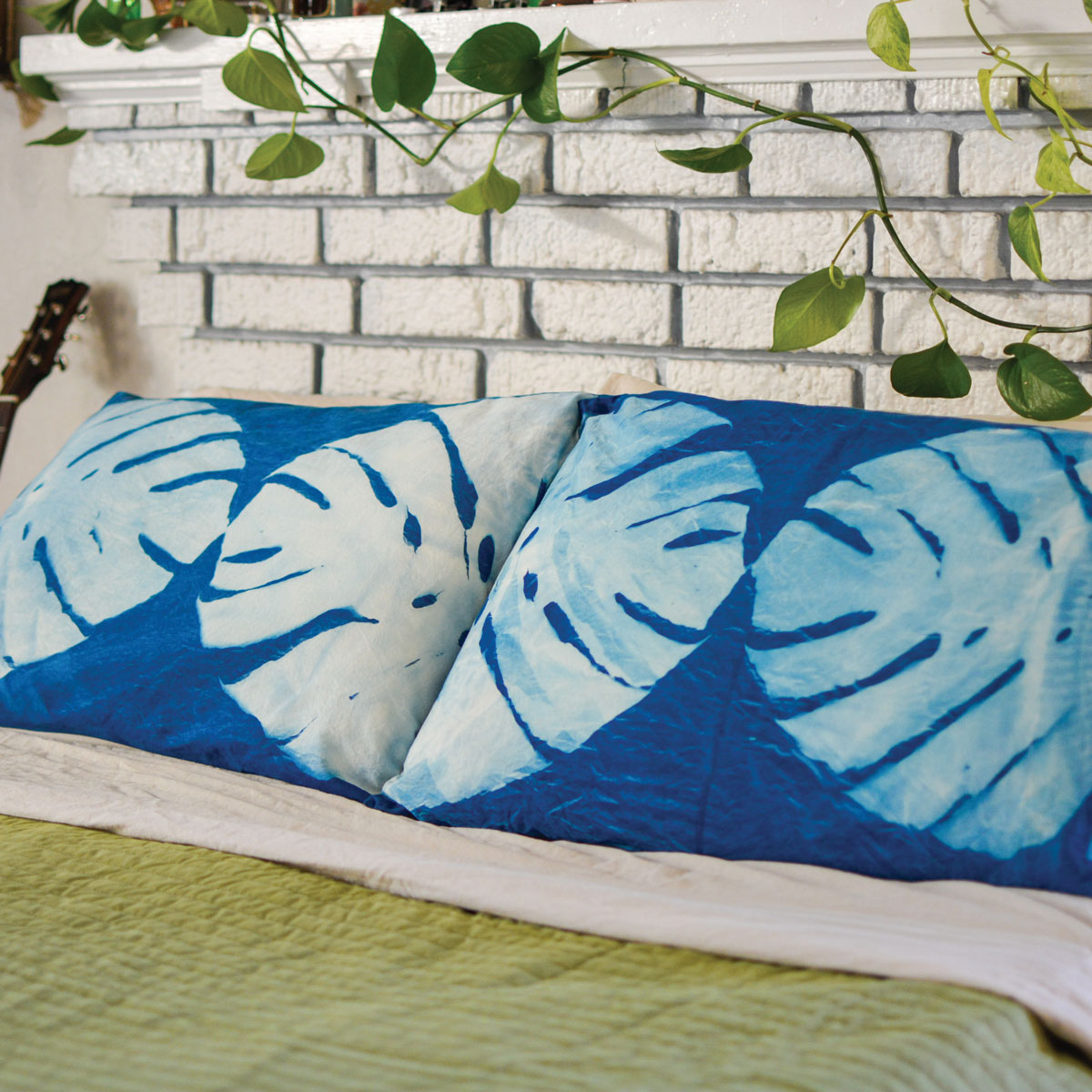Cyanotype print of tropical leaves on two pillowcases placed on a bed