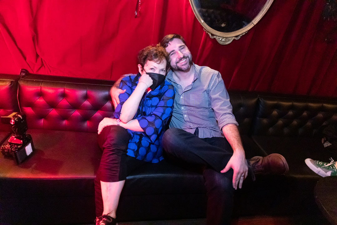 Photo of Meryl Meisler and a male fan sitting on a leather couch inside the club.