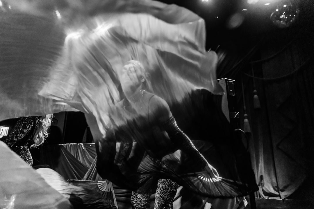 Black and white photo of a club performer waving the colored scarves causing a blur of movement in front of them.