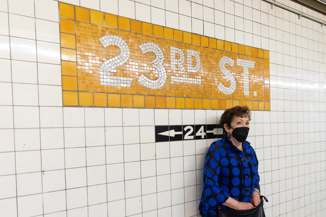 Photo of Meryl Meisler in the subway in front of a tiled wall that reads 23rd St..