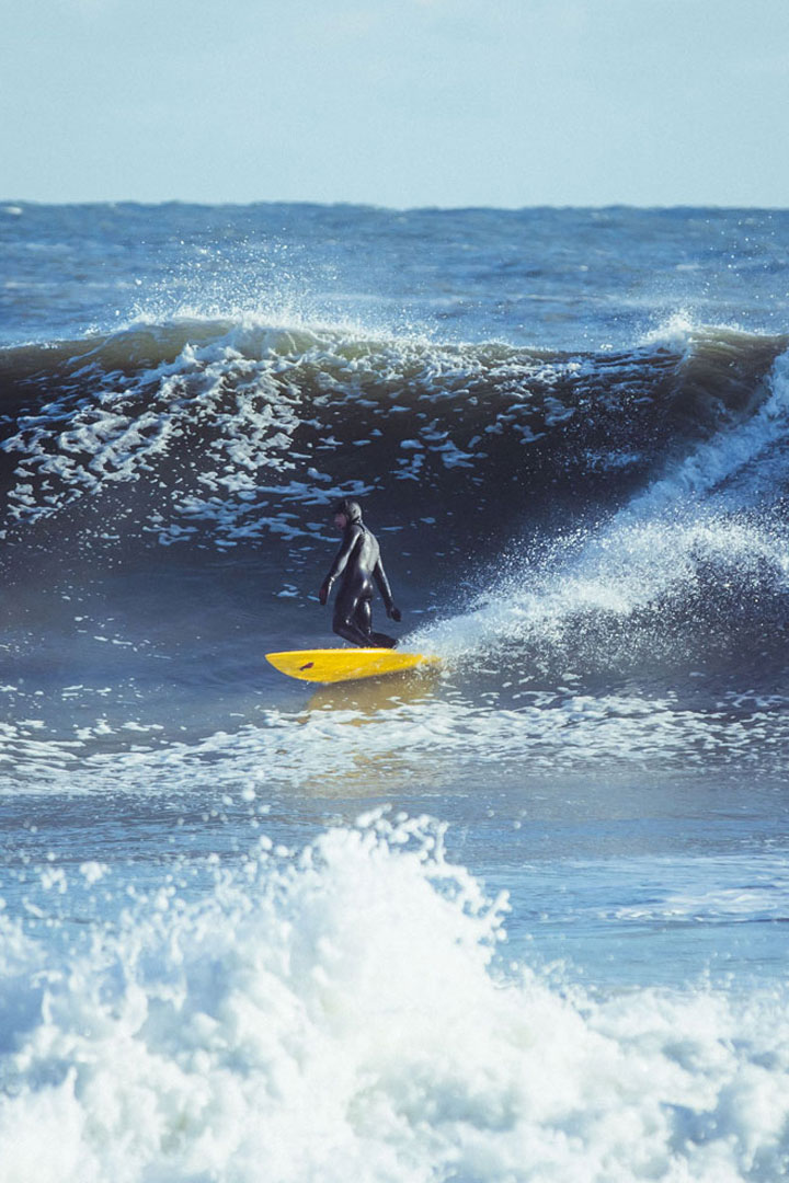 Photo of a surfer in a wetsuit riding a yellow surfboard in the waves.