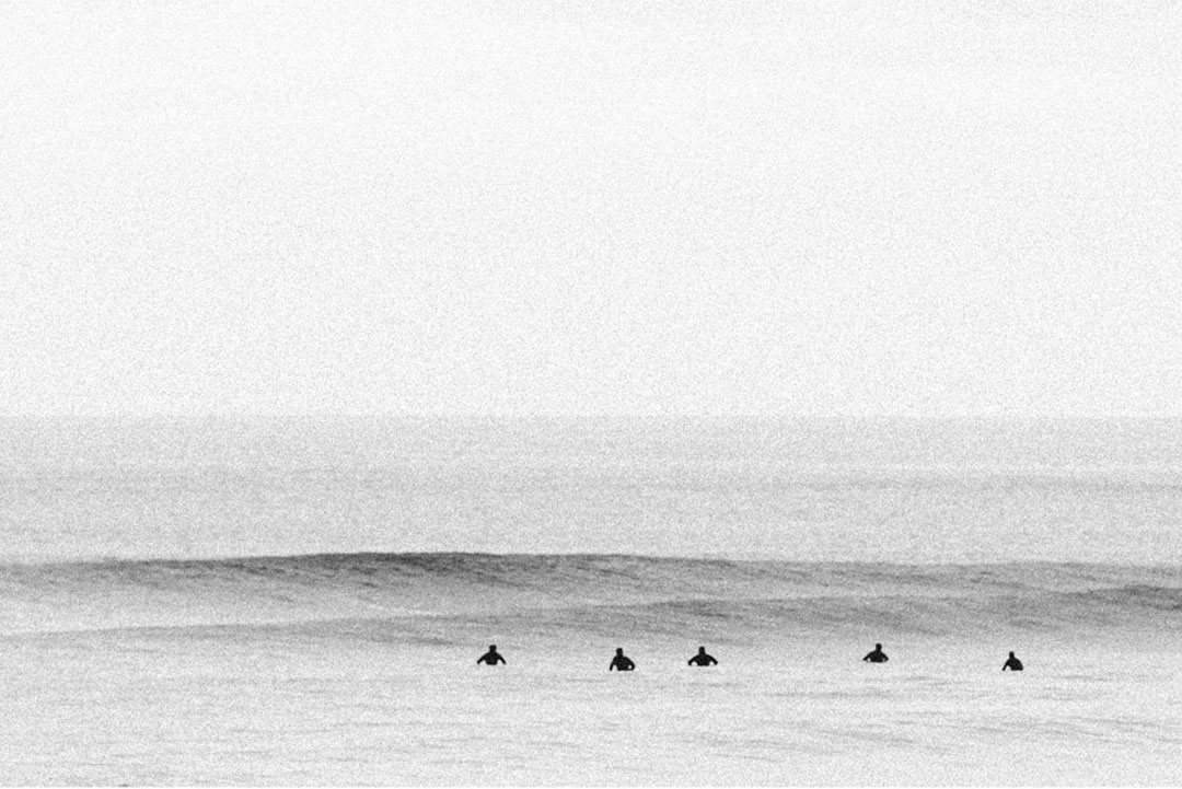Black and white photo of a group of surfers sitting in the ocean together waiting for a wave.